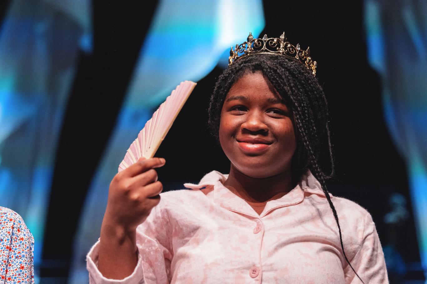 An LC2 (Year 8) CLC pupil holds and fan and wears a crown while performing in a production of 'Toy Box Tales' in the Parabola Arts Centre theatre