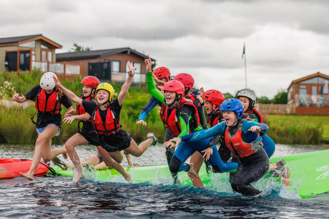 A group of nine CLC students wearing helmets and lifejackets leap joyfully into the water while on their LC3 (Year 9) Camp