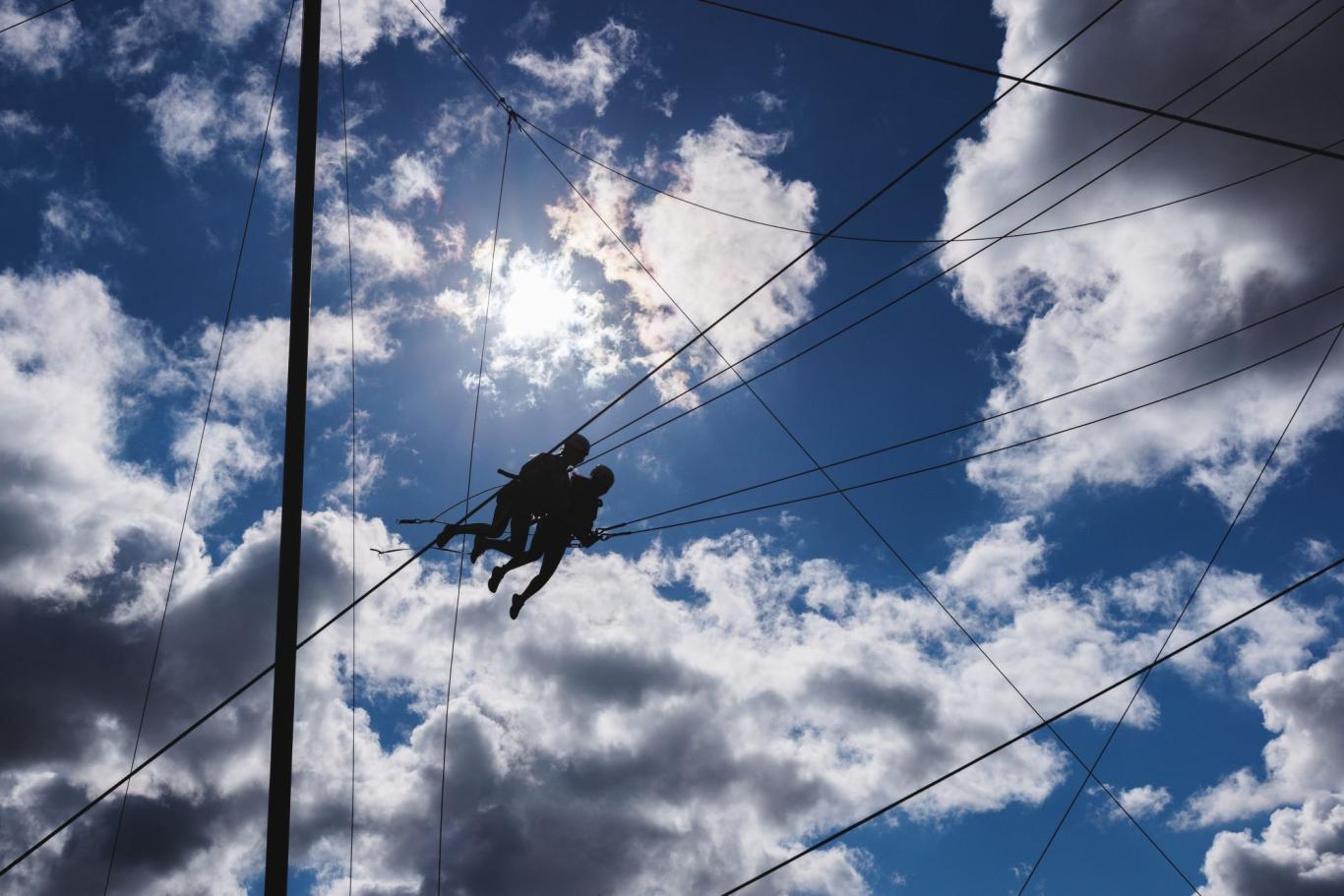 Silhouettes of two CLC students, set against a cloudy sunlit sky, as they jump during a rope course on a school adventure day