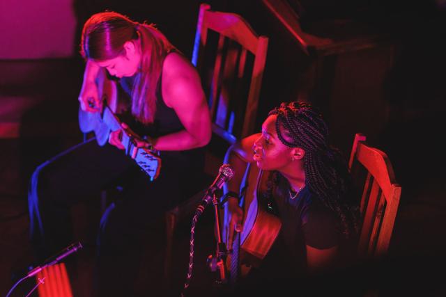 Two students playing guitar illuminated by soft colourful lighting