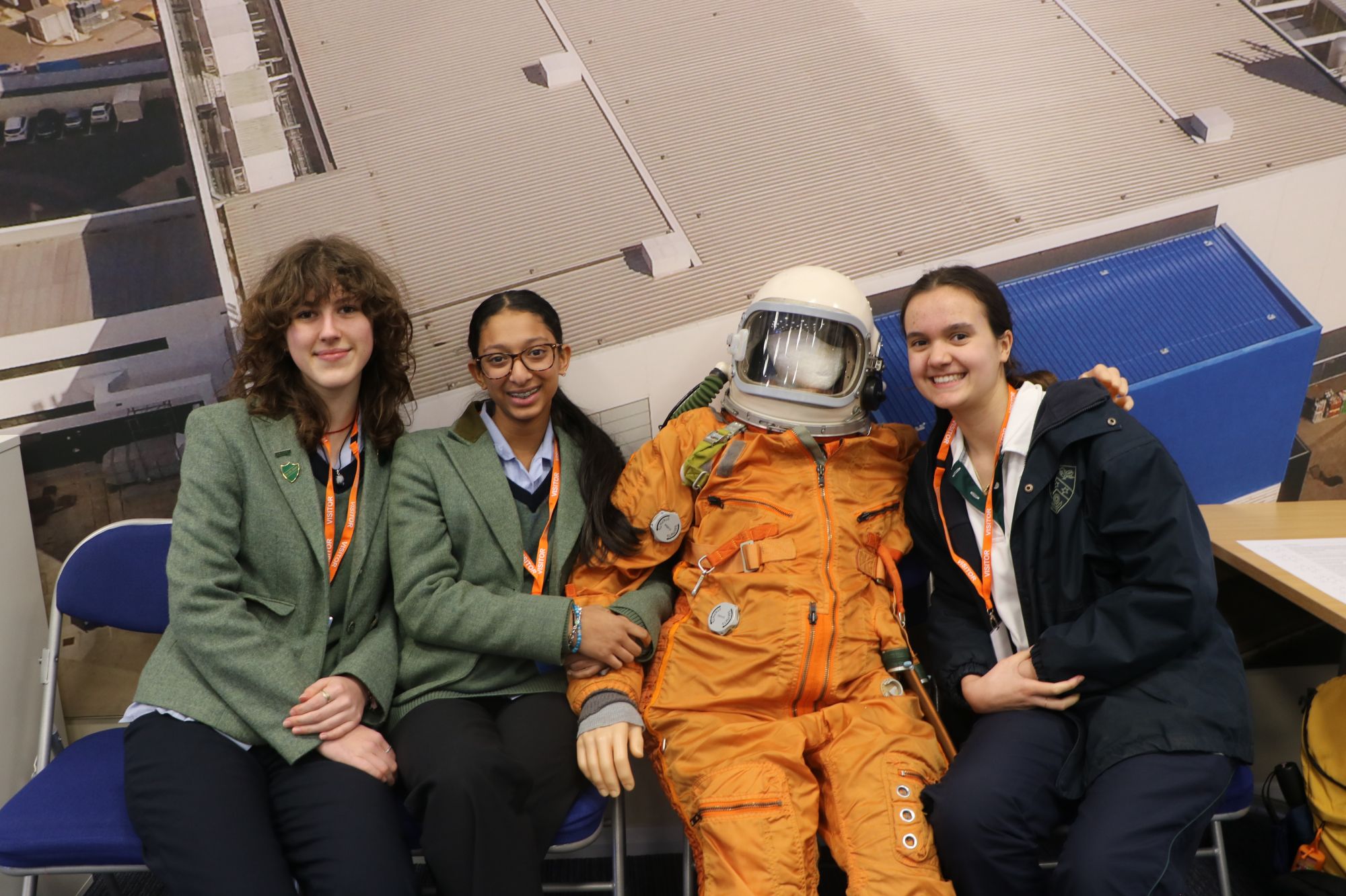 Three CLC students sit next to a dummy wearing an orange space outfit