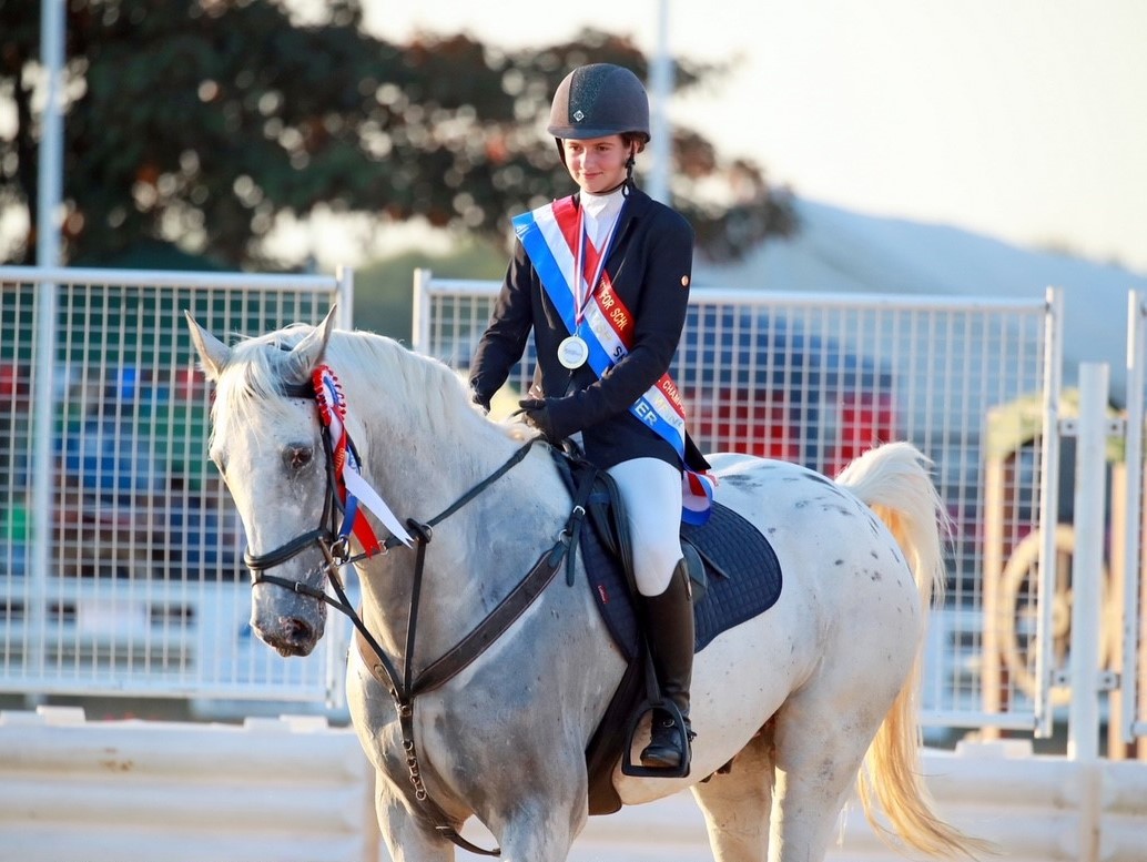 Lily riding her horse while wearing a winner's sash and medal